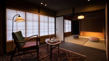 A traditional Japanese room with tatami flooring, a low table with tea set, a chair, and a lamp.