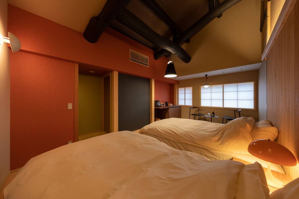 A hotel room with two beds, a kitchenette, and a large window with blinds.