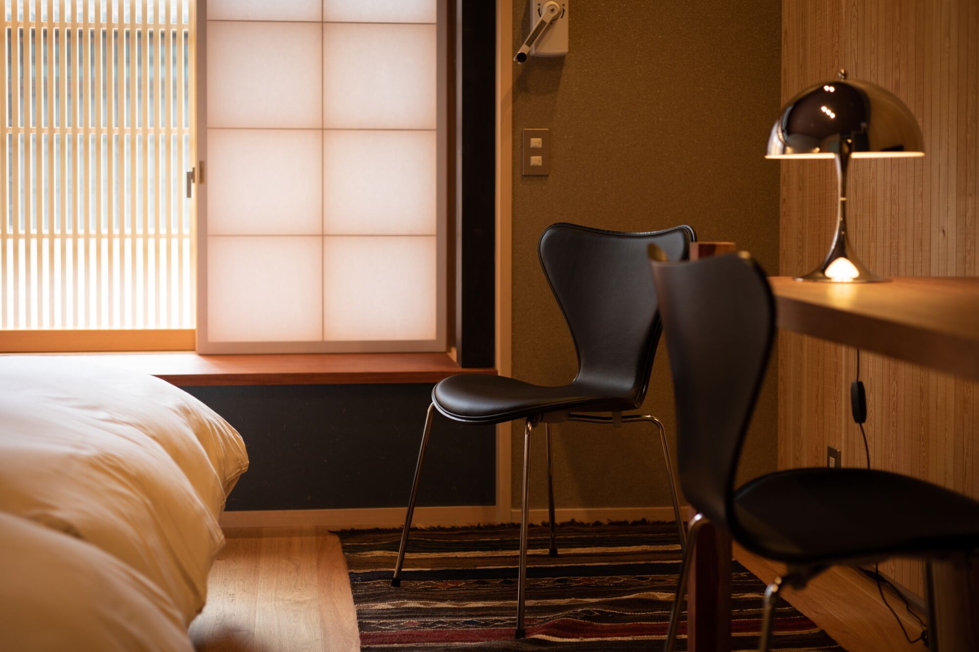 A hotel room with a bed, a desk with a lamp, and a chair.