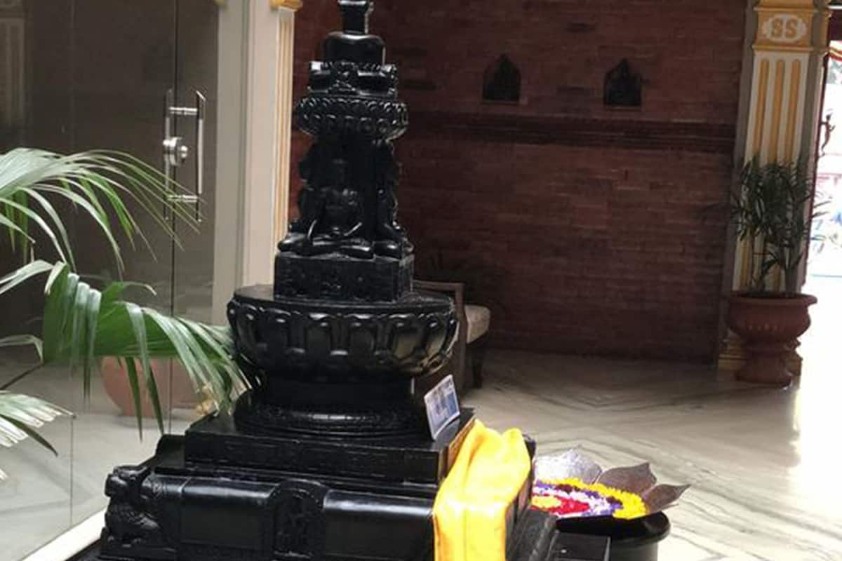 A black statue with a yellow cloth, a brick wall, and a potted plant.