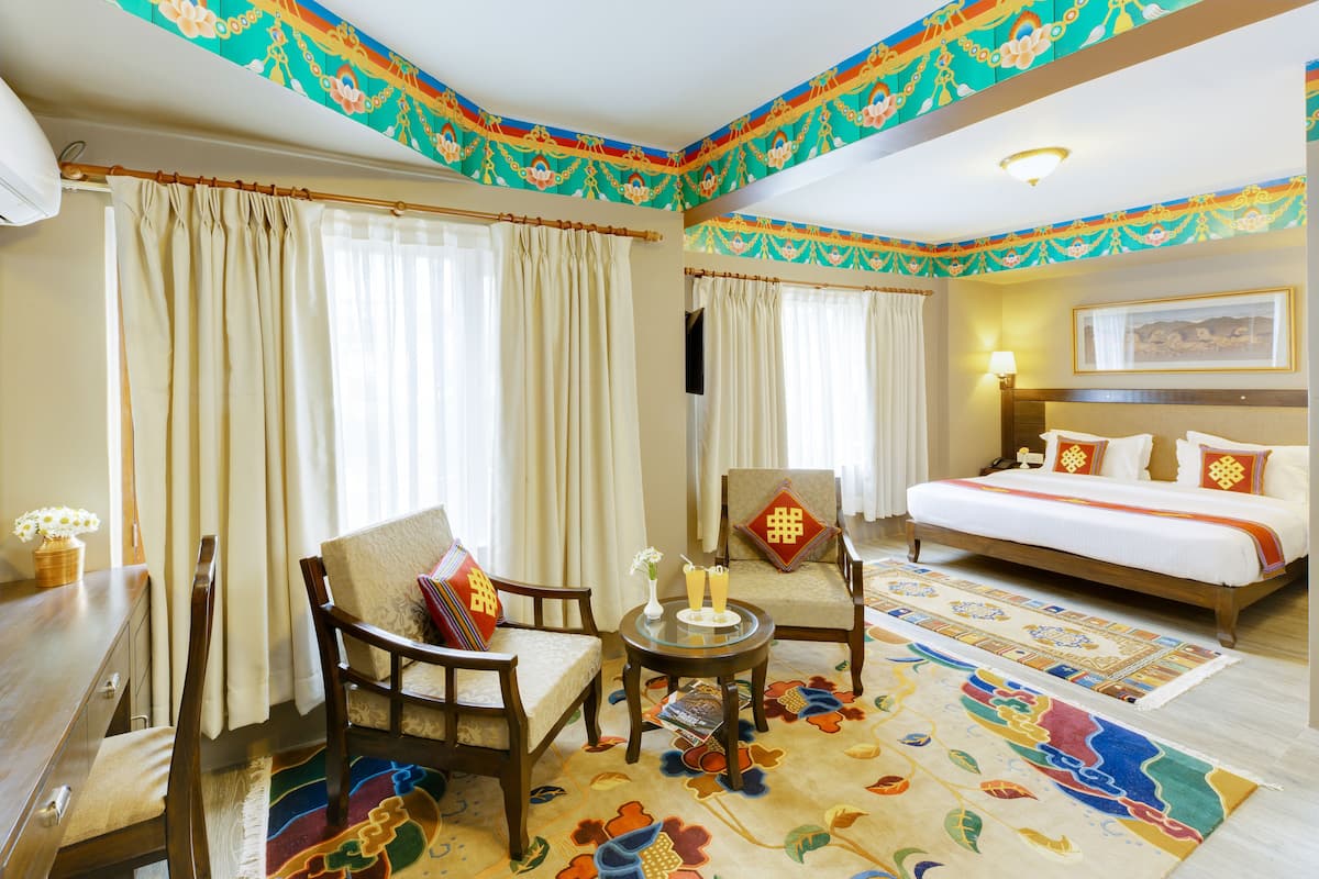 A hotel room with a bed, two chairs, a small table, and a decorative rug.