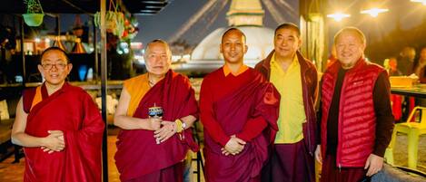 A group of monks in traditional robes standing in front of a temple with a large stupa in the background.