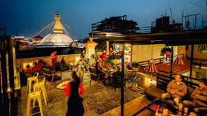 An outdoor seating area with tables and chairs, a large illuminated dome structure in the background, and a view of the cityscape. - Hotel Lotus Gems (Kathmandu)
