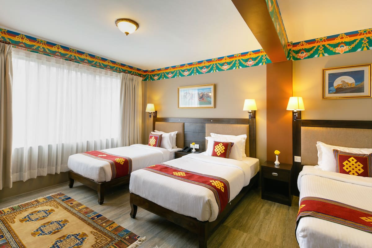 A hotel room with two beds, a nightstand, a lamp, a painting, and a window with curtains.