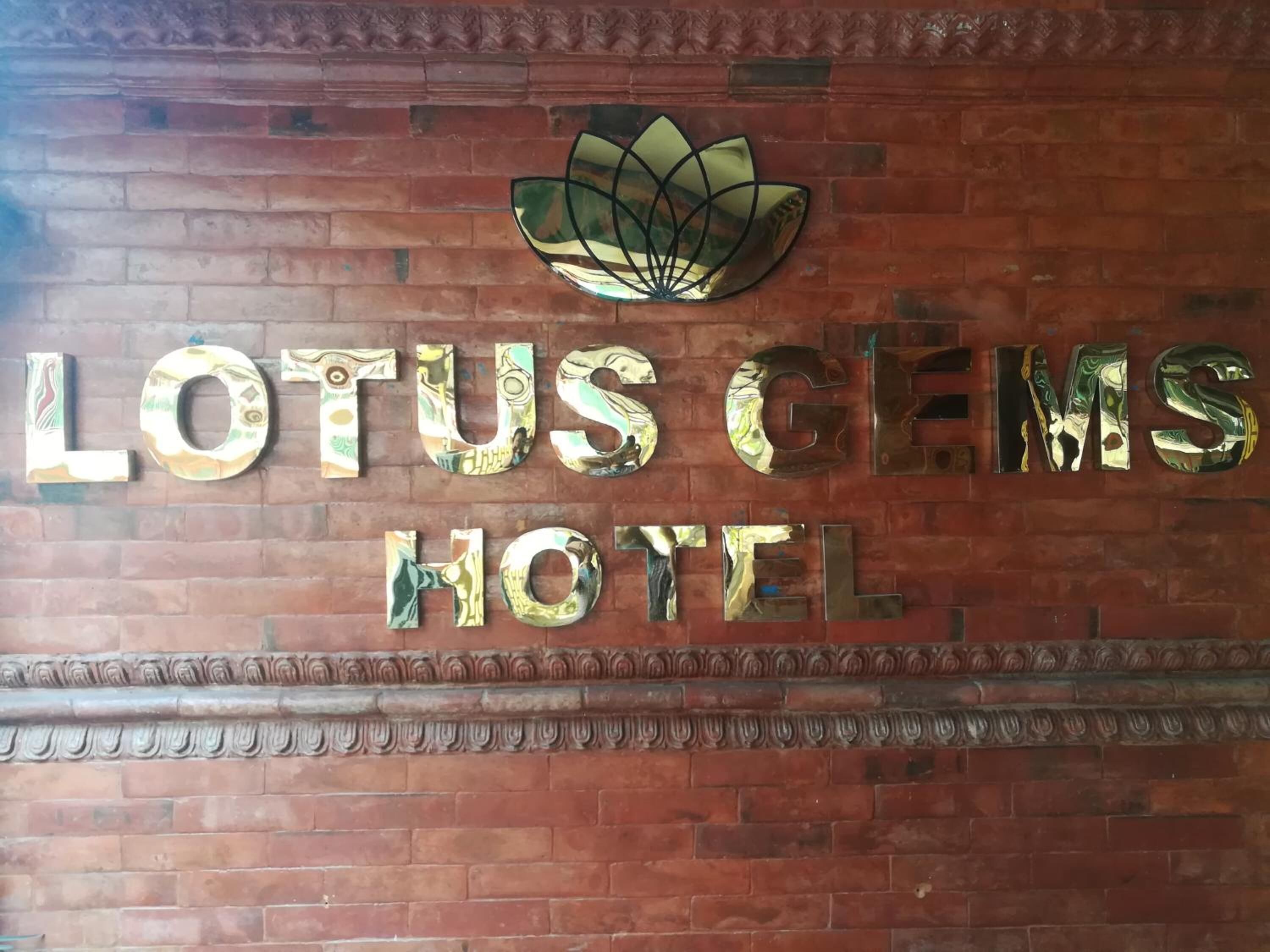 A brick wall with the words 'LOTUS CEMS HOTEL' in reflective metal letters.