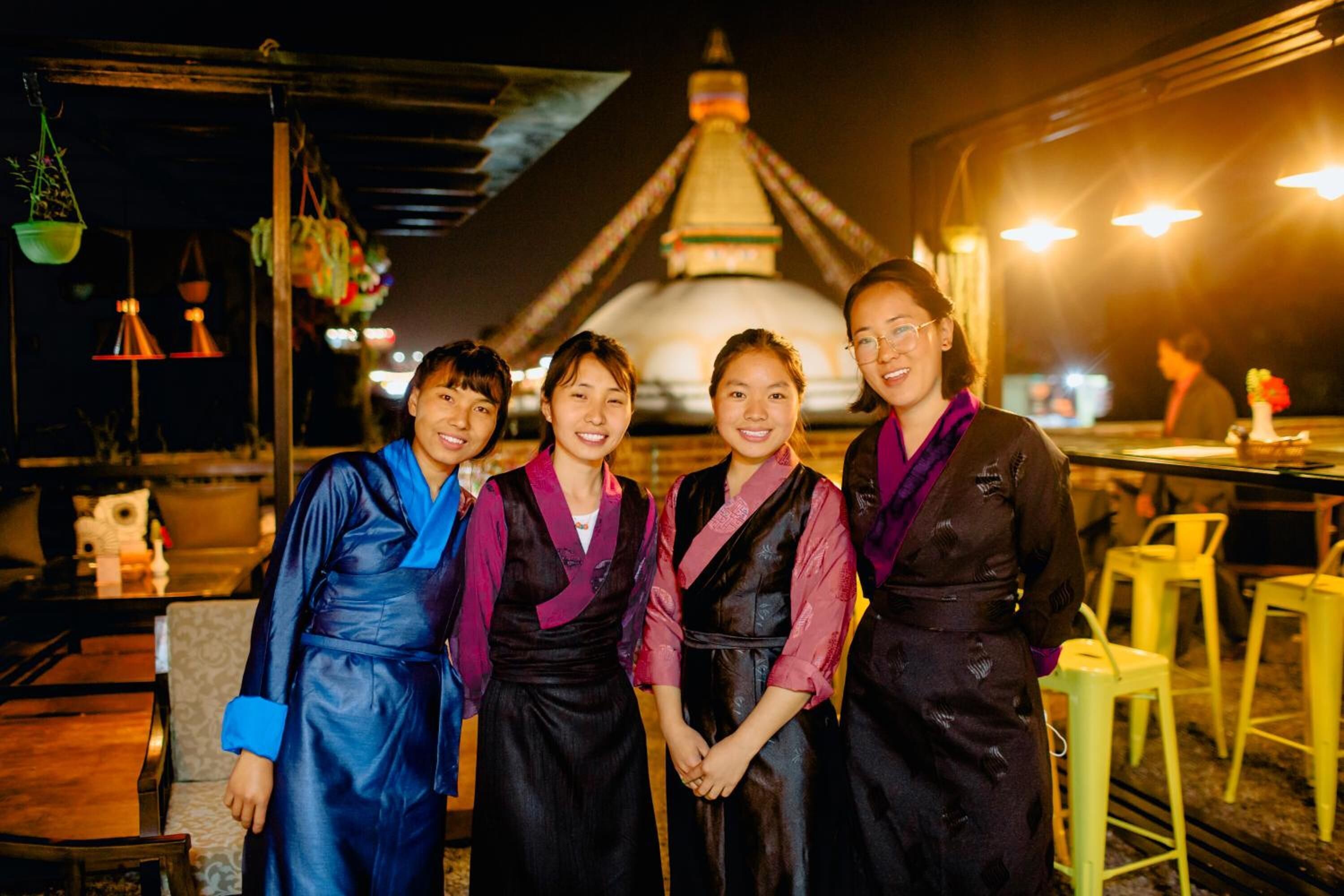A group of people in traditional attire standing in front of a building with a distinctive roof structure.