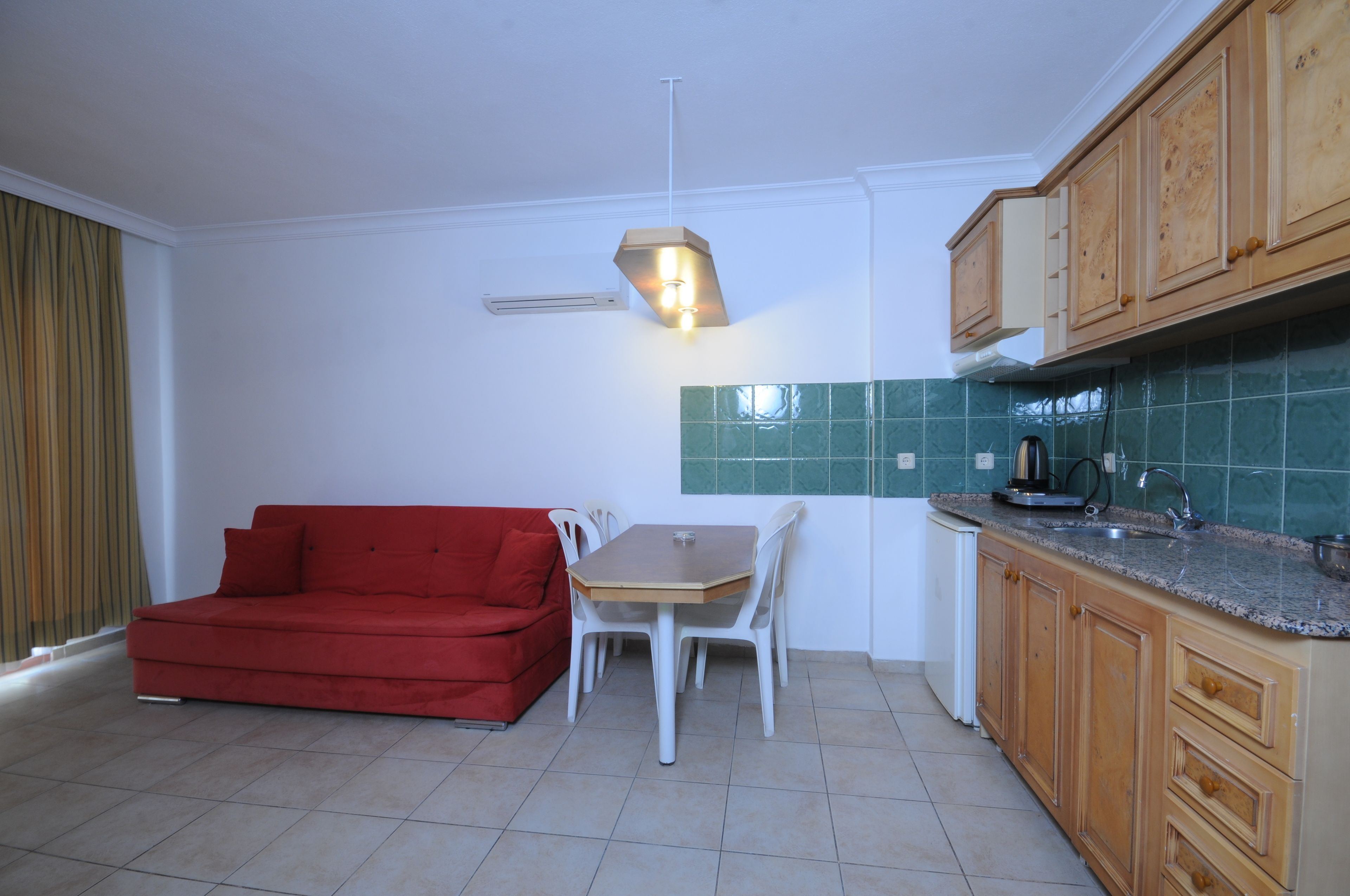 A compact kitchen with a dining table and chairs, a red sofa, and wooden cabinets.