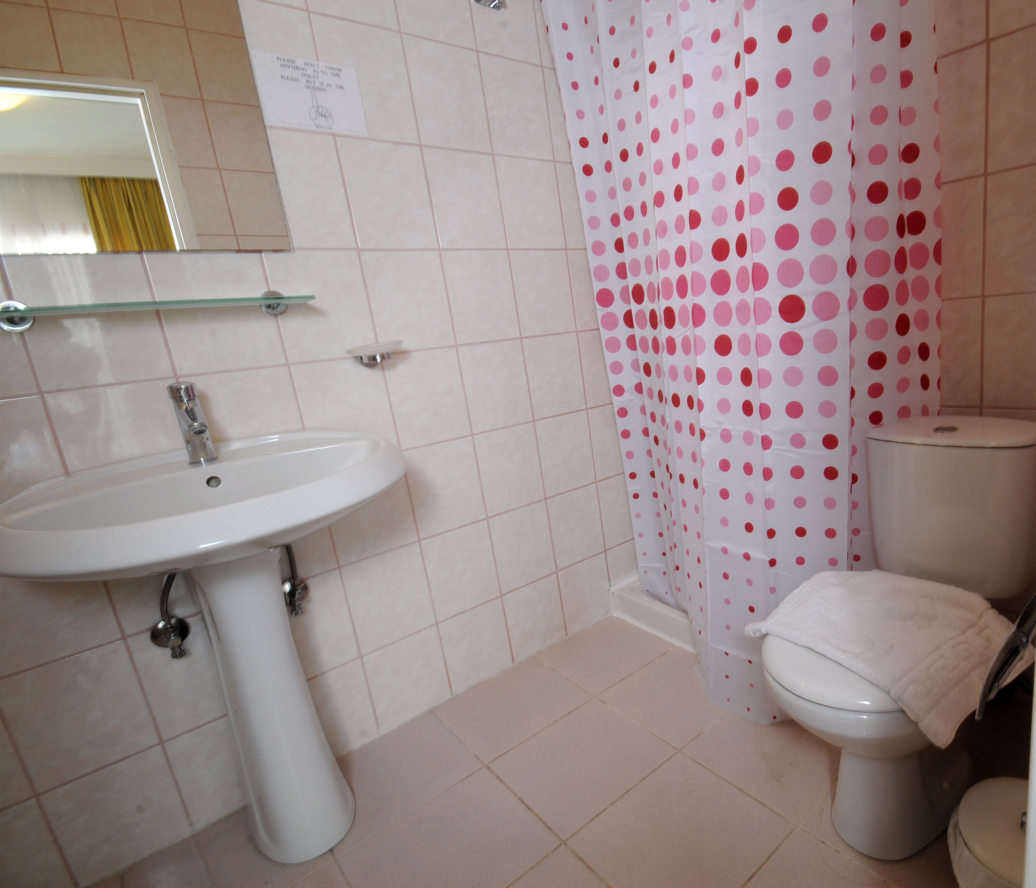 A bathroom with a white sink, a toilet, and a shower curtain with pink polka dots.