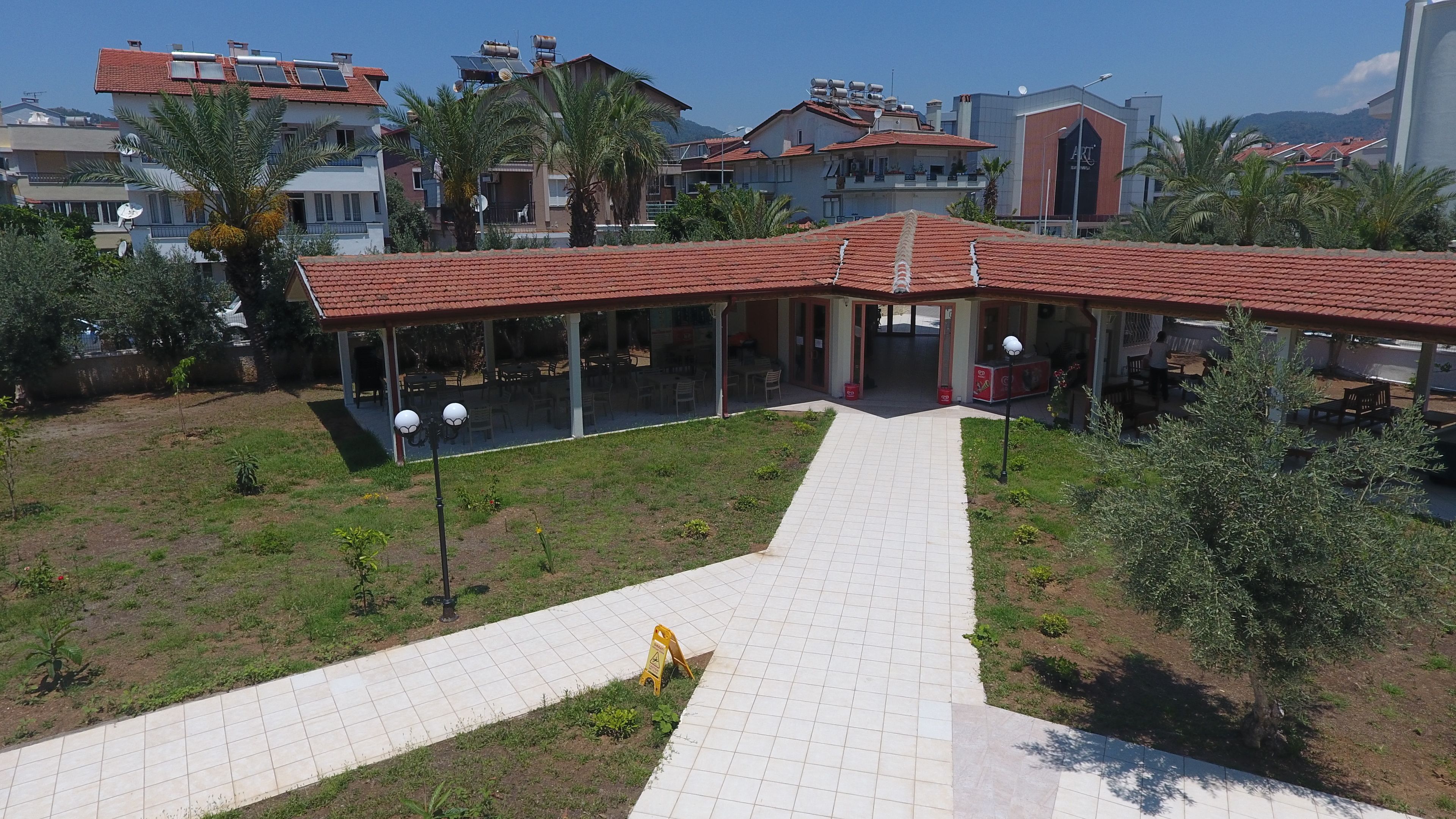 A building with a red-tiled roof, a covered outdoor seating area, and a paved walkway leading to the entrance.