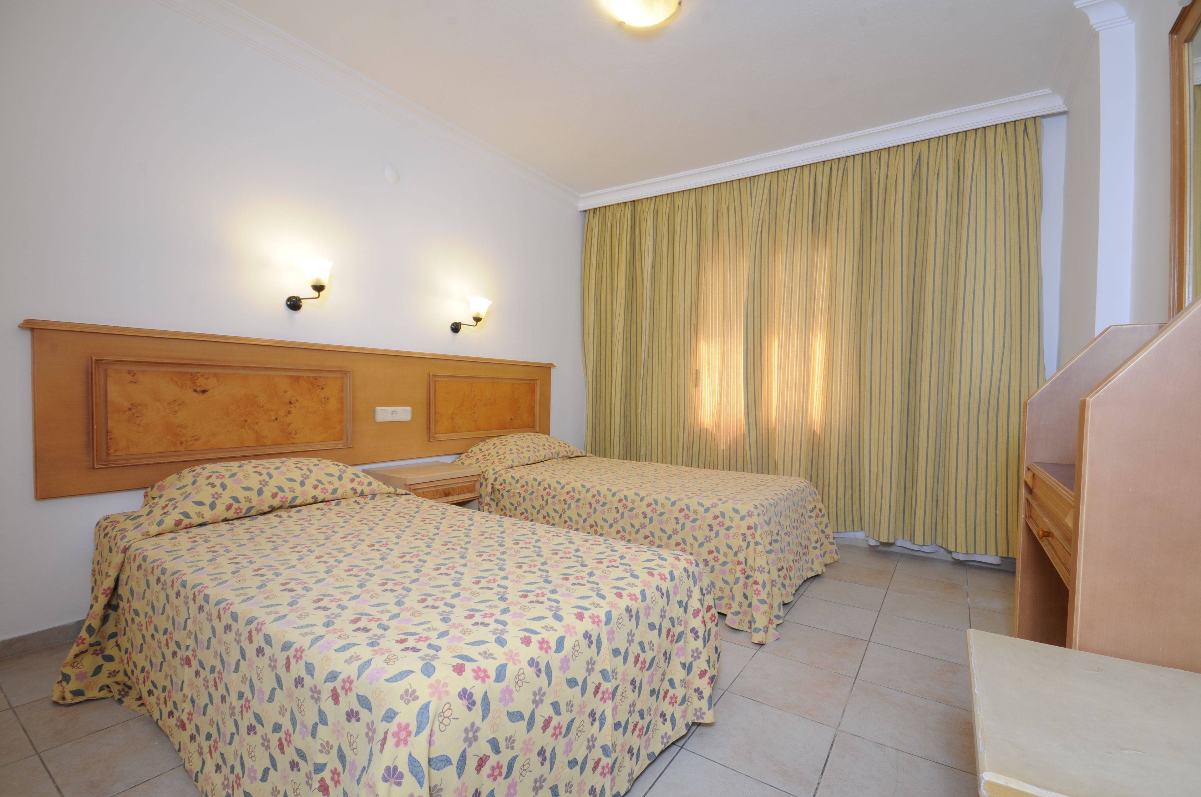 Una camera d'albergo con due letti, una testiera in legno, una piccola scrivania e una tenda.