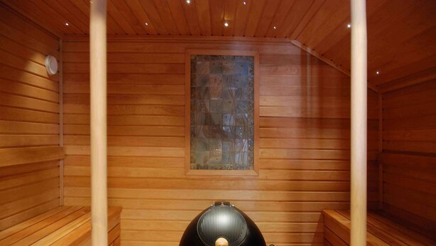 Un sauna aux murs en bois, doté d’une fenêtre en verre et d’un appareil de chauffage noir.