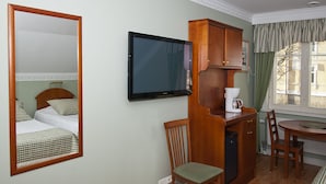 Habitación de hotel con cama, televisor, aparador de madera, silla, mesa y ventana con cortinas.
