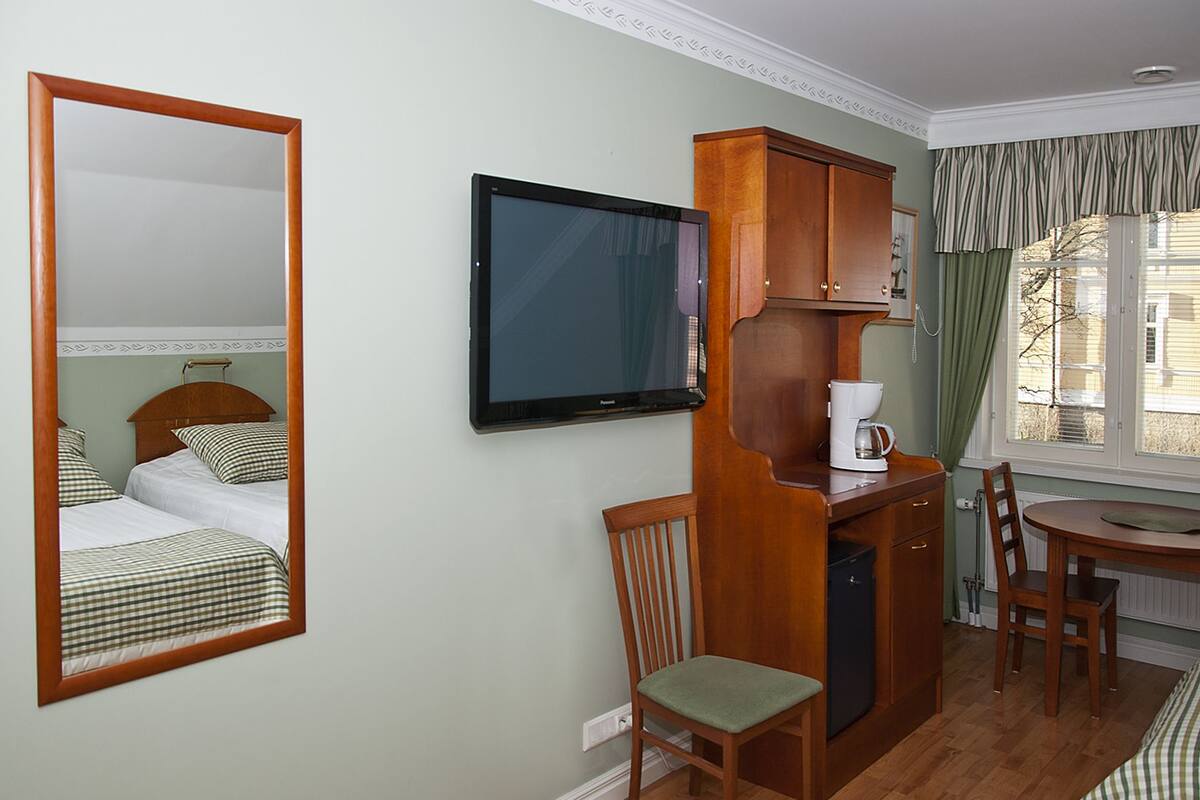 A hotel room with a bed, a television, a wooden cabinet, a chair, a table, and a window with curtains.