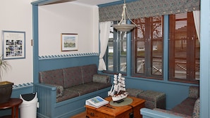 Una habitación con paneles azules, un sofá estampado, un aparador de madera y un modelo de barco encima.