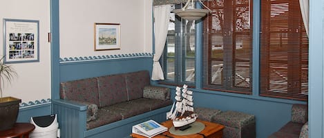 Una habitación con paneles azules, un sofá estampado, un aparador de madera y un modelo de barco encima.