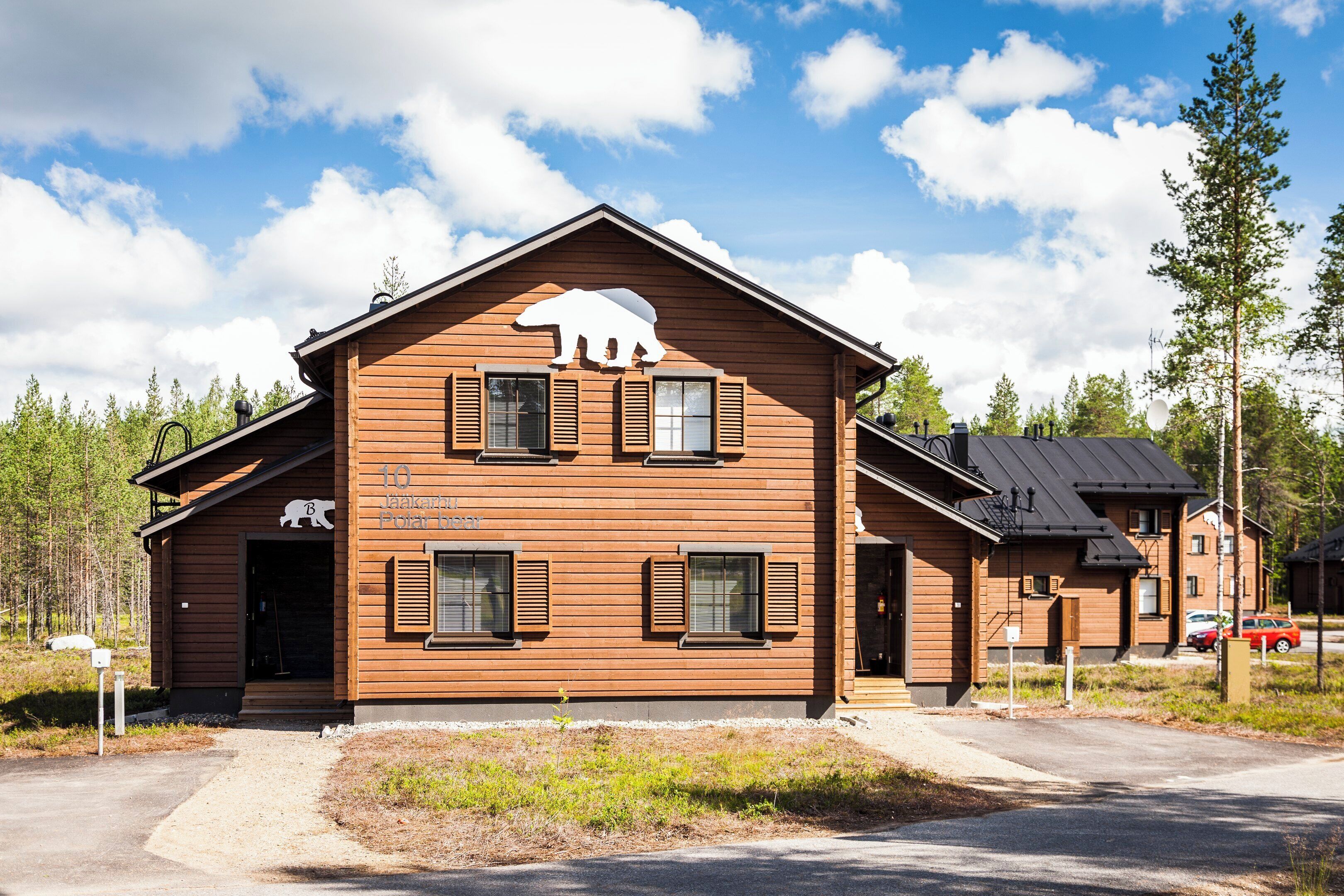En træhytte med bjørnlogo, en veranda og en kort indkørsel.