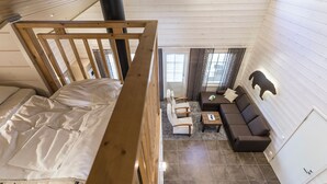 A loft-style bedroom with a wooden bunk bed, a small seating area with a sofa and chairs, and a large window providing natural light. - Ranua Resort Holiday Villas (Ranua)