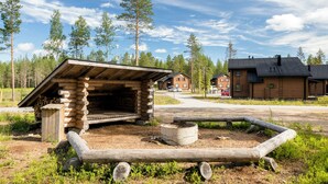A rustic cabin with a sloped roof and a chimney, surrounded by a wooden fence and a fire pit. - Ranua Resort Holiday Villas (Ranua)