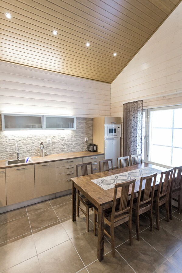 A modern kitchen with a wooden countertop, built-in microwave, and a dining area with a wooden table and chairs. - Ranua Resort Holiday Villas (Ranua)