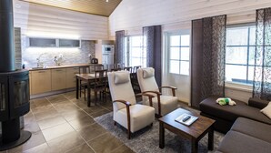 A modern living room with a fireplace, a sofa, a coffee table, and a dining area with chairs and a kitchen in the background. - Ranua Resort Holiday Villas (Ranua)