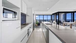 A modern kitchen with a view of the city, a dining area with a table and chairs, and a large window. - Circle on Cavill - Q Stay (Surfers Paradise)