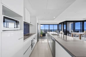 A modern kitchen with a view of the city, a dining area with a table and chairs, and a large window. - Circle on Cavill - Q Stay (Surfers Paradise)