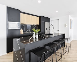 A modern kitchen with a black countertop, stainless steel appliances, and a wooden cabinet. - Circle on Cavill - Q Stay (Surfers Paradise)