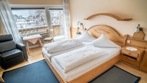 A hotel room with a large bed, a chair, a small table, and a view of a balcony. - Gasthaus & Naturparkhotel Linde (Löffingen)
