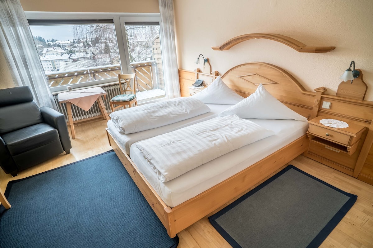 Une chambre d’hôtel avec un grand lit, une chaise, une petite table et une vue sur un balcon.