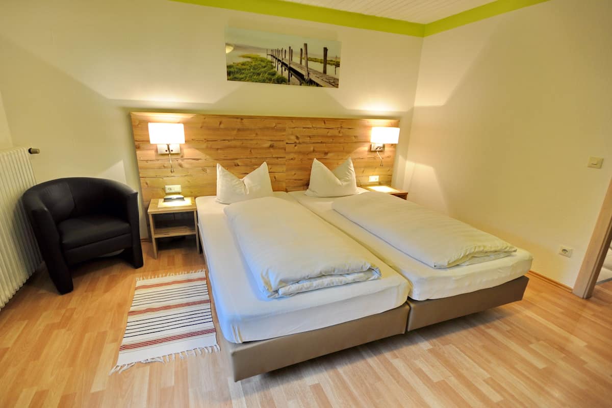 Un lit double avec une tête de lit en bois, deux tables de chevet avec des lampes, une chaise noire et un tapis à rayures.