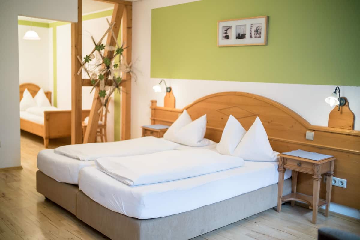 Un lit double avec du linge de lit blanc, une tête de lit en bois, une table de chevet avec une lampe et un tableau encadré au mur.