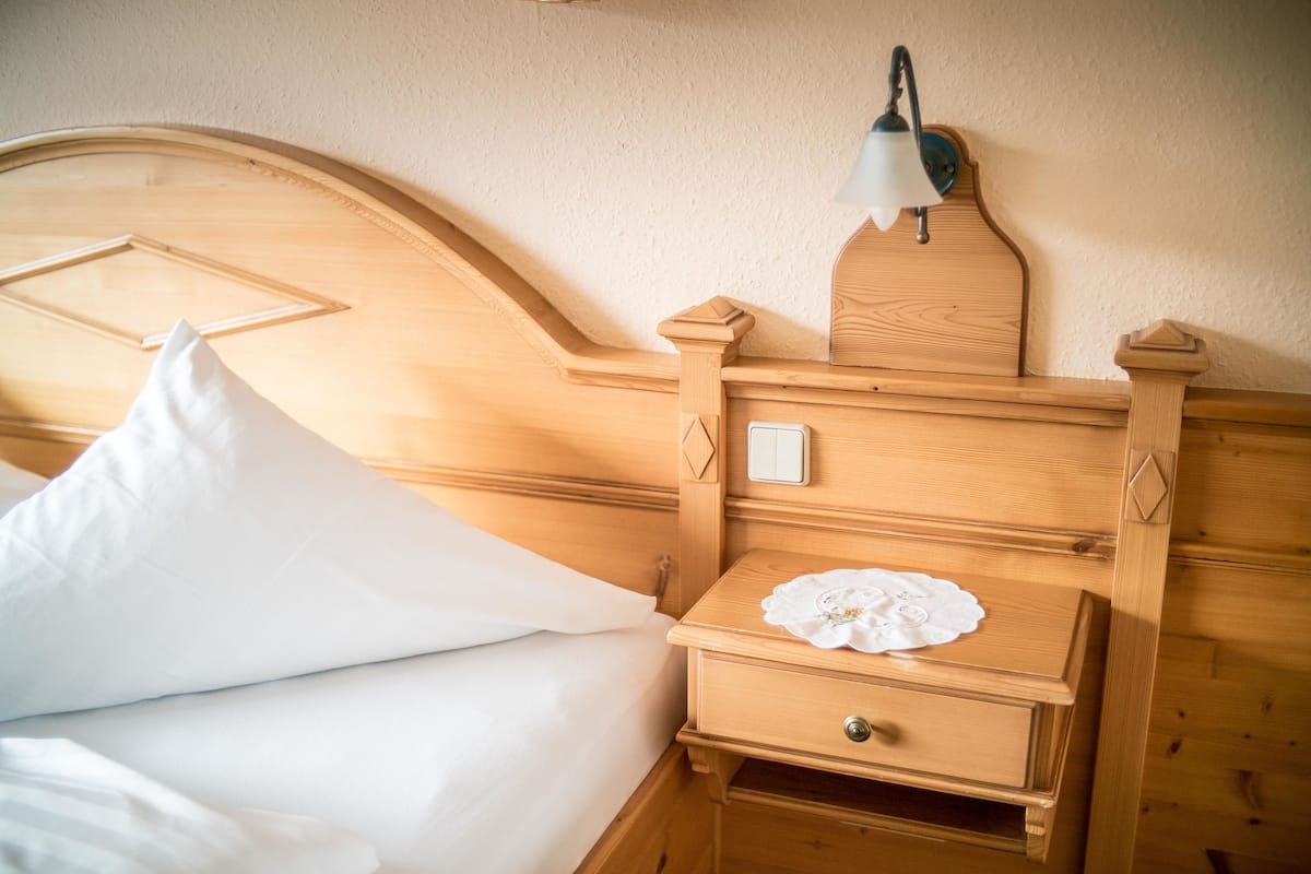 Un lit en bois avec un oreiller blanc et une table de chevet dotée d’une lampe et d’un tiroir.