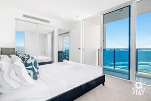 A modern hotel room with a large bed, a balcony with ocean views, and a sliding glass door. - H'Residences - Q Stay (Surfers Paradise)