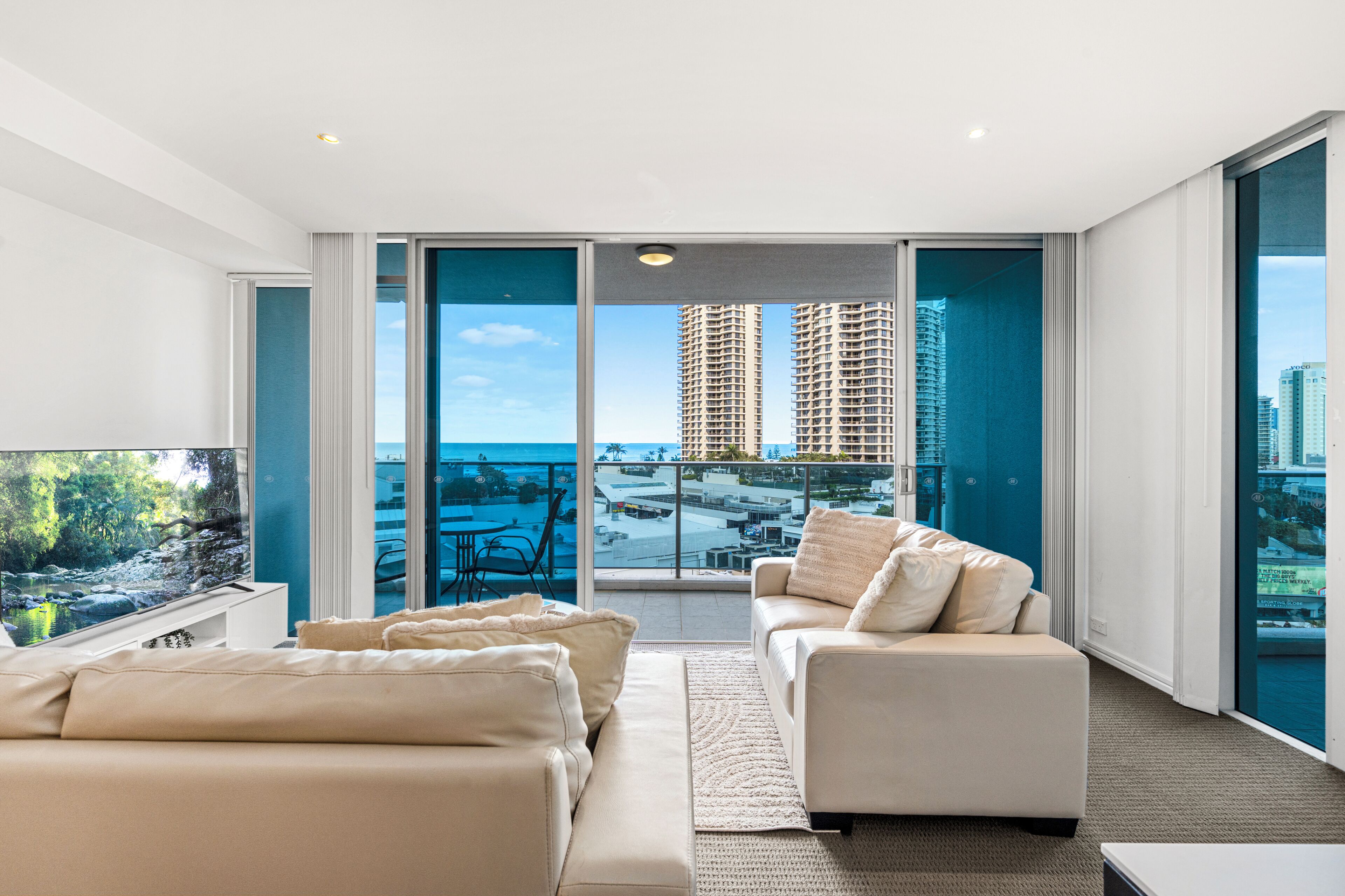 A modern living room with a large window, a sofa, and a view of tall buildings.