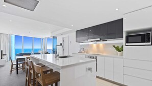 A modern kitchen with a large island, dark cabinets, and a microwave.