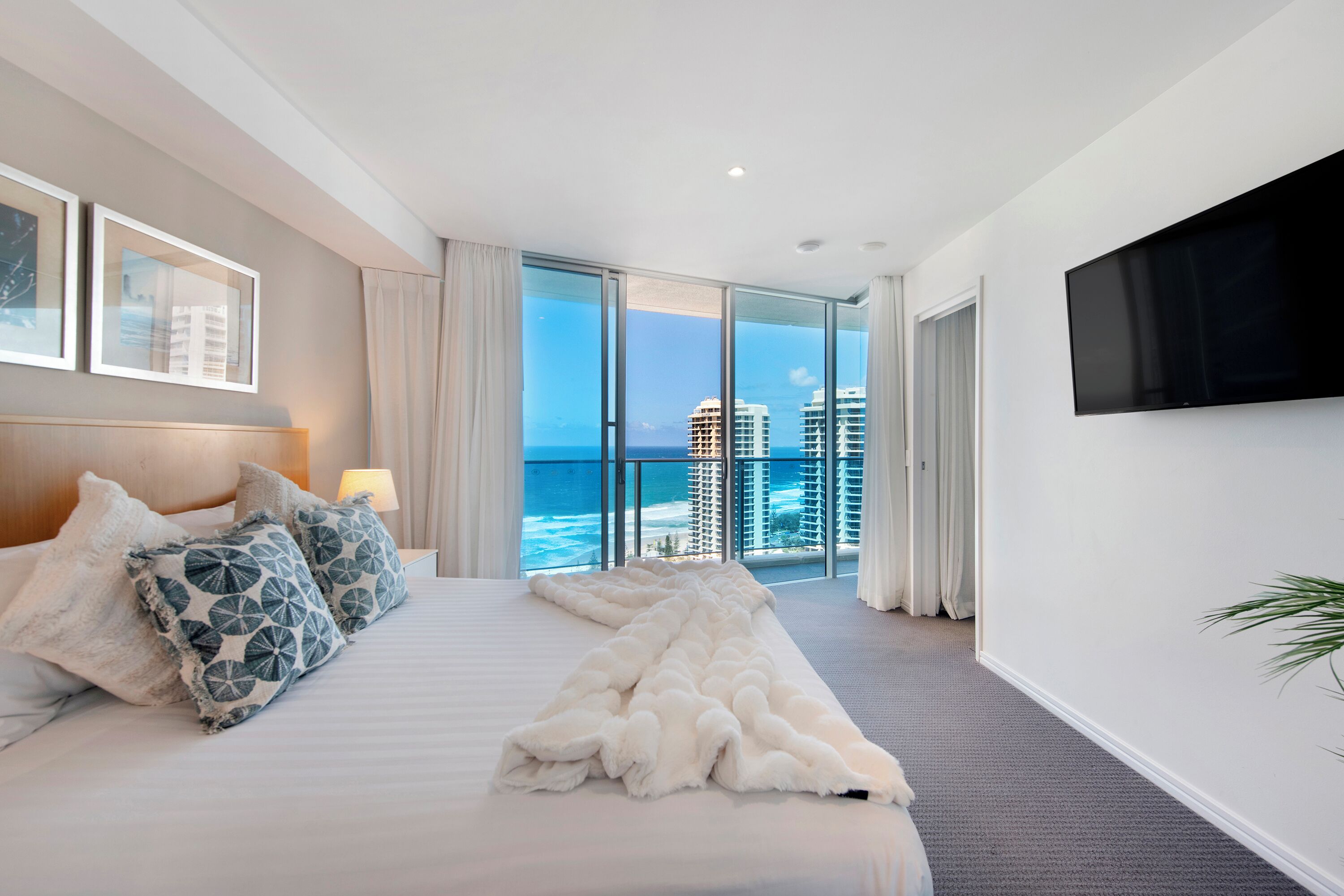 A hotel room with a large bed, a TV mounted on the wall, and a view of the ocean.