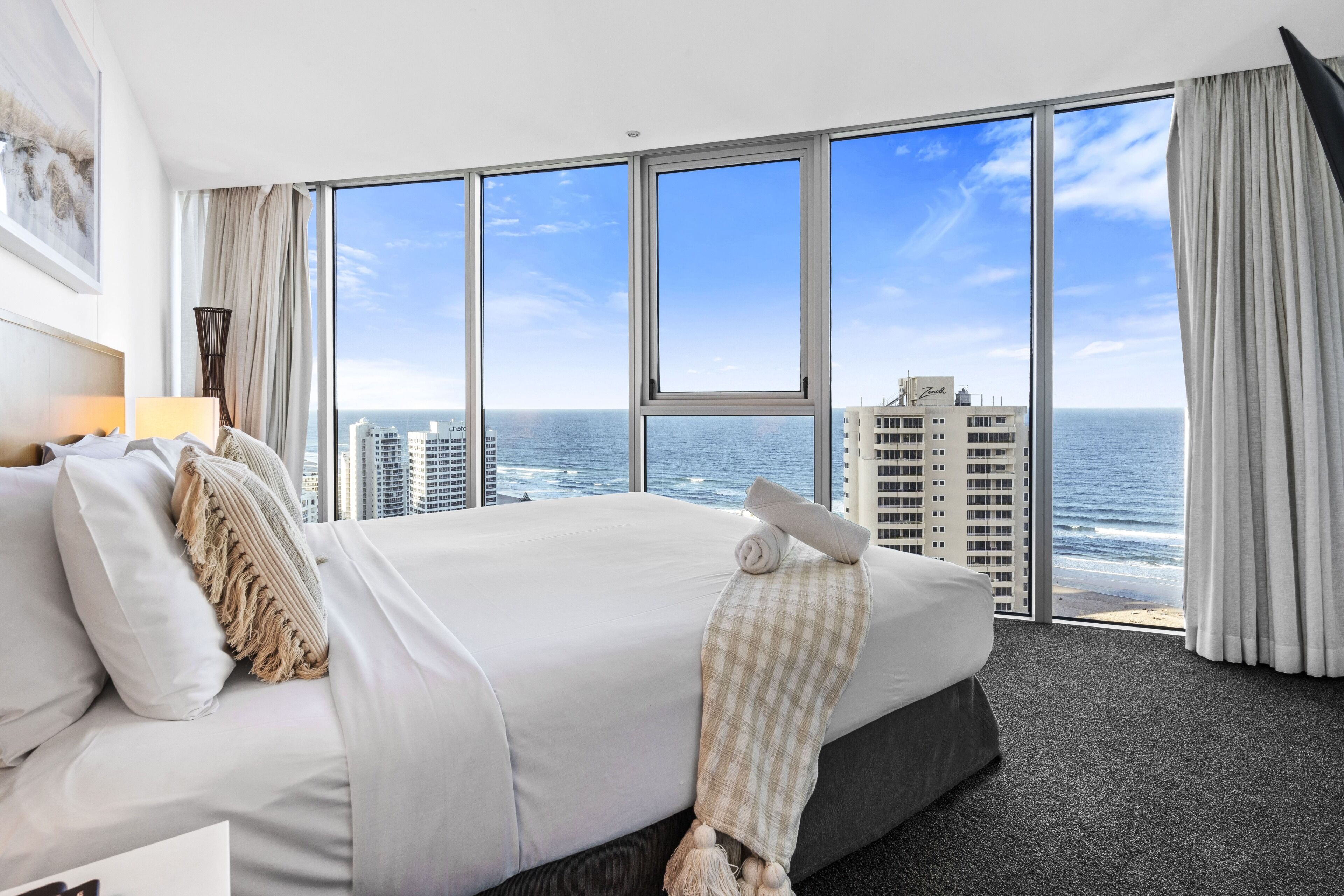 A hotel room with a large bed, a view of the ocean, and a cityscape.