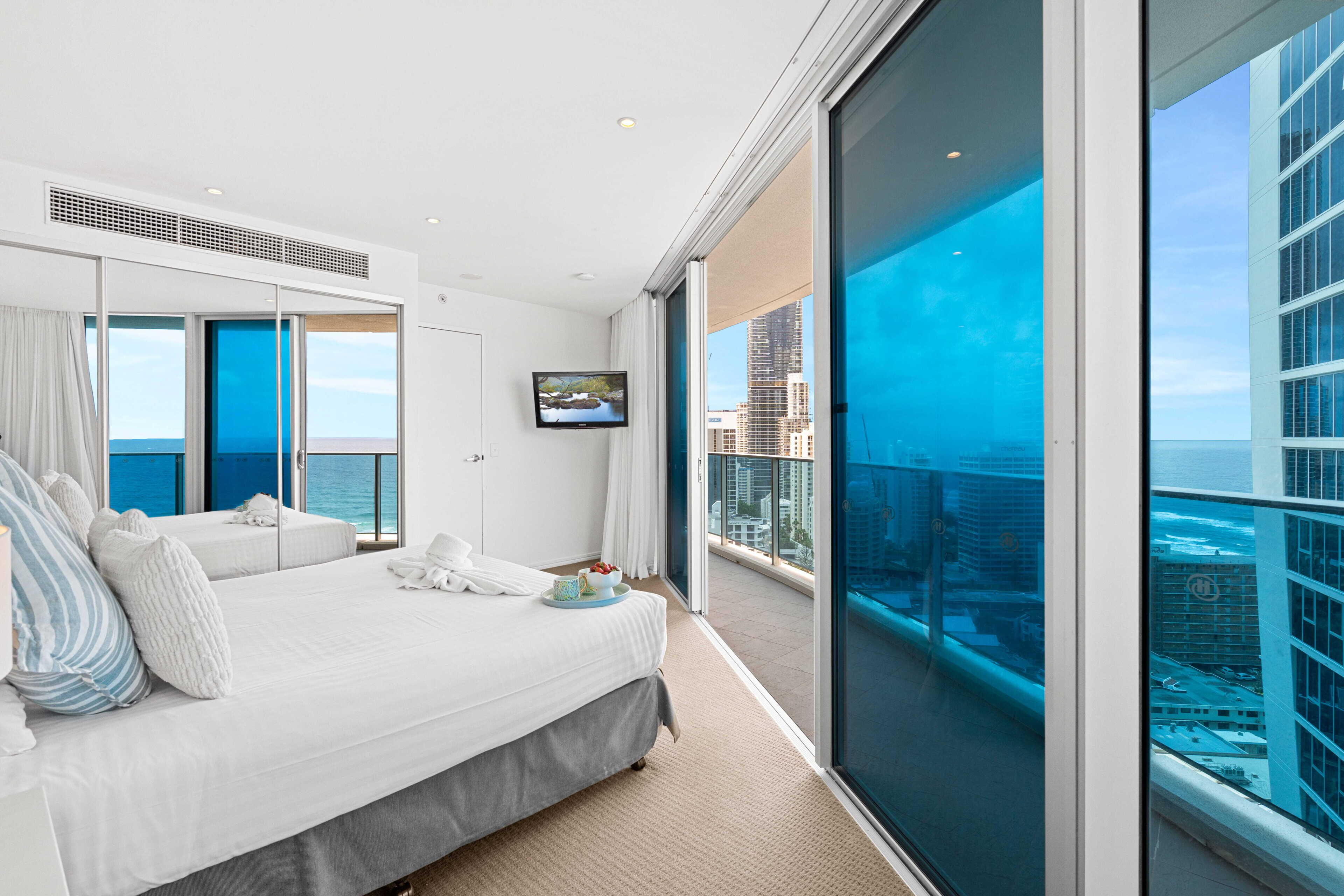 A modern hotel room with a large bed, a television, and a balcony with a city view.