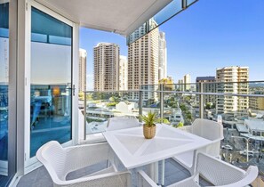 A balcony with a table and chairs, a potted plant, and a city view with tall buildings. - H'Residences - Q Stay (Surfers Paradise)