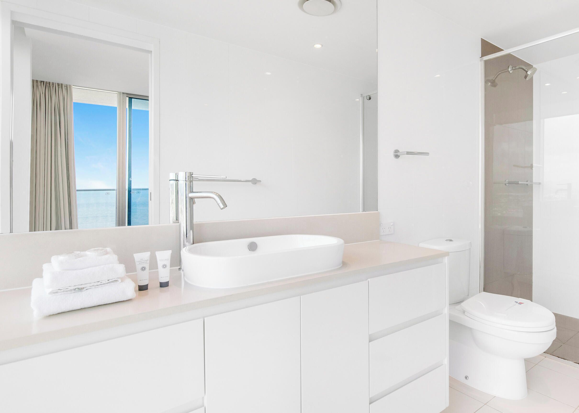 A modern bathroom with a large mirror, a white sink, a toilet, and a shower.