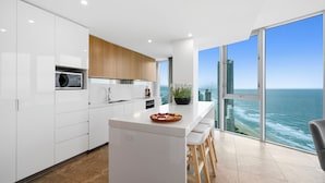 A modern kitchen with white cabinets, a central island, and a view of the ocean. - H'Residences - Q Stay (Surfers Paradise)