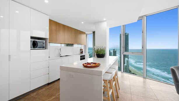 A modern kitchen with white cabinets, a central island, and a view of the ocean.