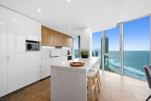 A modern kitchen with white cabinets, a central island, and a view of the ocean. - H'Residences - Q Stay (Surfers Paradise)