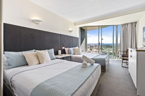 Habitación de hotel con dos camas, un escritorio, una silla y un ventanal con vistas a la ciudad.