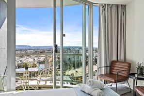 Un balcon donnant sur le paysage urbain, un lit avec vue, une chaise et une petite table avec une plante.