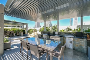 An outdoor patio with a glass-top table and wicker chairs, a stone wall, and a statue.