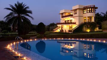Una casa moderna de dos pisos con piscina, rodeada de jardines cuidados y palmeras.