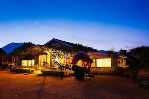 A house with a large window, a wheelbarrow, and a person bending over. - Pushkar Resort (Pushkar)