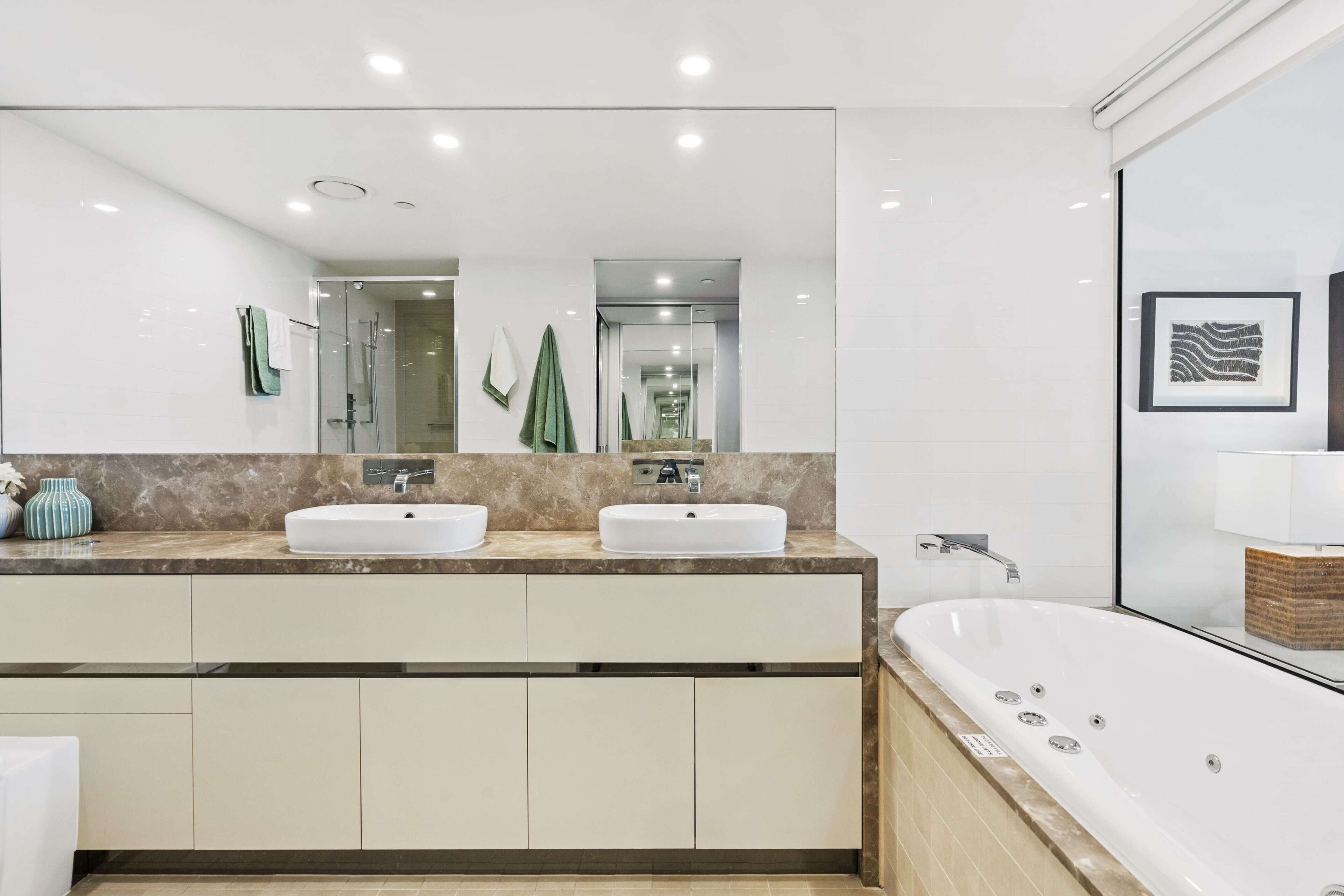 Une salle de bain moderne avec deux lavabos, une grande baignoire et un miroir décoré d’œuvres d’art.