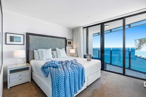 A bedroom with a large bed, a nightstand, a bedside lamp, a window with a view of the ocean, and a balcony with a railing. - Soul - Q Stay (Surfers Paradise)